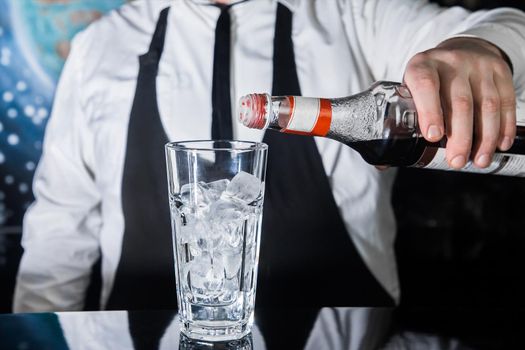 The hand of a professional bartender pours red syrup into a glass of ice cubes. The process of preparing an alcoholic cocktail.