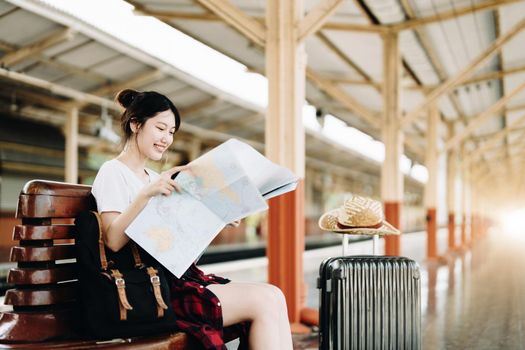 summer, relax, vacation, travel, portrait of a cute Asian girl looking at a map to plan a trip while waiting at the train station