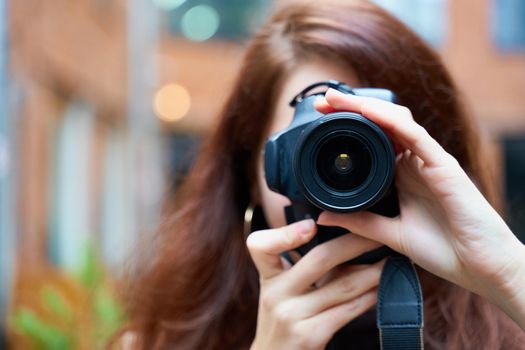 Beautiful stylish fashionable girl holds a camera in her hands and takes pictures. Woman photographer with long dark hair, copy space