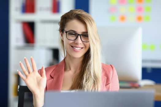 Portrait of pretty businesswoman greeting coworkers on video call in cabinet. Employee in suit, online meeting with colleagues. Corporate, business concept