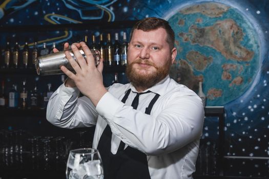 Professional bartender adult bearded Caucasian-looking portrait whipping up a cocktail in a shaker beverage making tool.