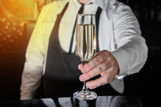 A professional bartender serves chilled champagne sparkling with gases in glass on the bar.