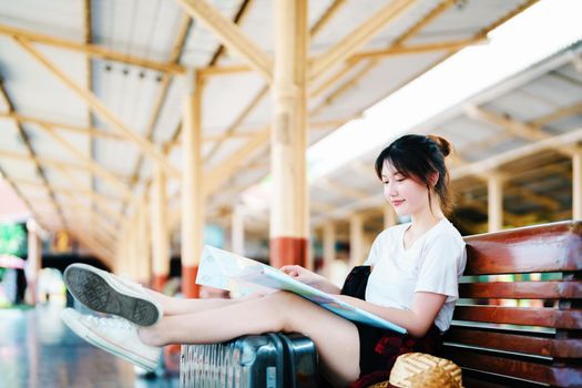 summer, relax, vacation, travel, portrait of a cute Asian girl looking at a map to plan a trip while waiting at the train station