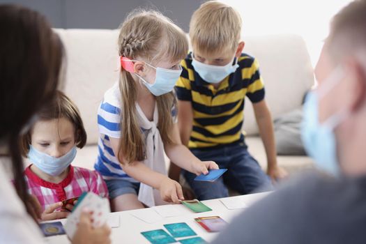 Portrait of kids in face masks, prevent virus spread in kindergarten, developing card game. Task for young generation, learn new things. Quarantine concept