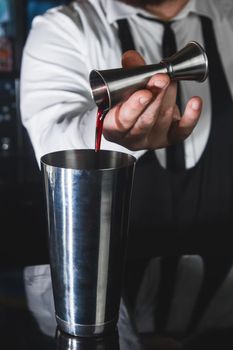 The hands of a professional bartender pour syrup into a measuring glass of jigger in a metal tool for preparing and, stirring alcoholic cocktails of shaker drinks.