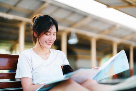 summer, relax, vacation, travel, portrait of a cute Asian girl looking at a map to plan a trip while waiting at the train station