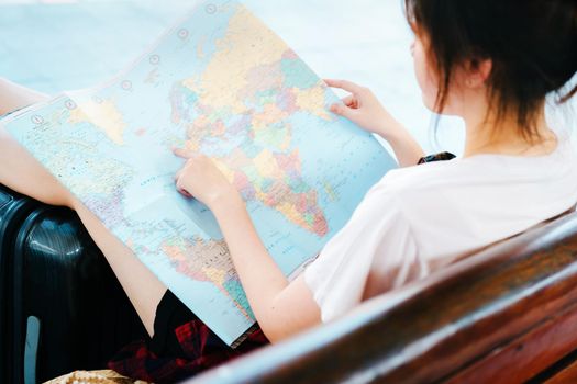 summer, relax, vacation, travel, portrait of a cute Asian girl looking at a map to plan a trip while waiting at the train station