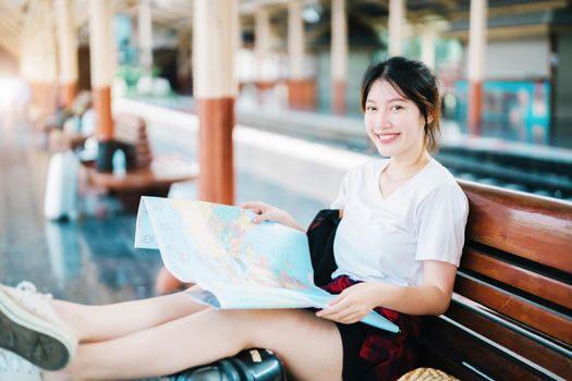 summer, relax, vacation, travel, portrait of a cute Asian girl looking at a map to plan a trip while waiting at the train station