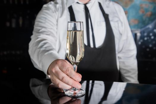 A professional bartender serves chilled champagne sparkling with gases in glass on the bar.