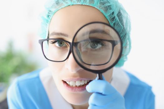 Portrait of doctor in glasses looks through magnifying loupe, intern provide investigation in clinic. Medical worker use magnifying glass. Medicine concept