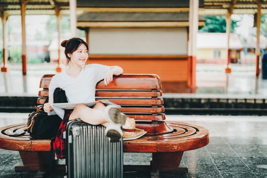 summer, relax, vacation, travel, portrait of a cute Asian girl looking at a map to plan a trip while waiting at the train station