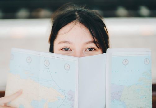 summer, relax, vacation, travel, portrait of a cute Asian girl looking at a map to plan a trip while waiting at the train station