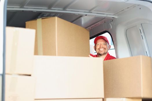 Portrait of happy smiling middle aged man on work, put cardboard boxes in truck for delivery. Cheerful male help with relocation. Delivery service concept