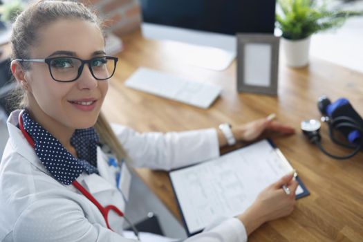 Portrait of doctor fill in patients medical history, stethoscope on neck, modern clinic office. Professional specialist with qualification. Health concept