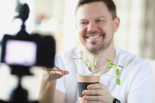 Portrait of middle aged man recording on video how he growing plants at home. Fan of botany, new hobby. Video blogger, social media, technology concept
