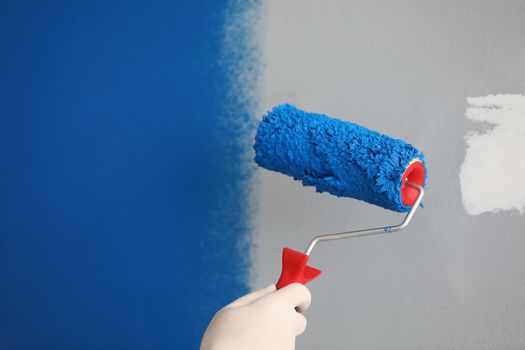 Close-up of worker with roller tool ready to paint walls, cover in blue colour. Wall with part white and blue lac. Renovation, design, redecoration concept