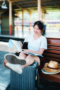 summer, relax, vacation, travel, portrait of a cute Asian girl looking at a map to plan a trip while waiting at the train station