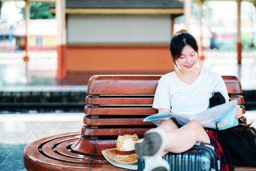 summer, relax, vacation, travel, portrait of a cute Asian girl looking at a map to plan a trip while waiting at the train station