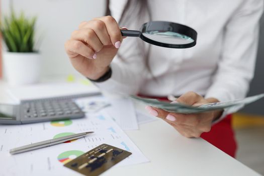 Close-up of female hold magnifying glass analyzing business financial data, manager calculates company finances. Money to invest, corporate profit concept