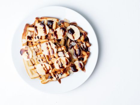 Belgian curd waffles with raspberries, banana, chocolate syrup. Breakfast with tea on white background, top view, copy space