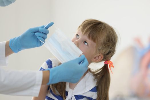 Portrait of doctor put face mask on kid face to protect from virus spread. Little girl sit in hospital and get checkup. Medicine, covid prevention concept