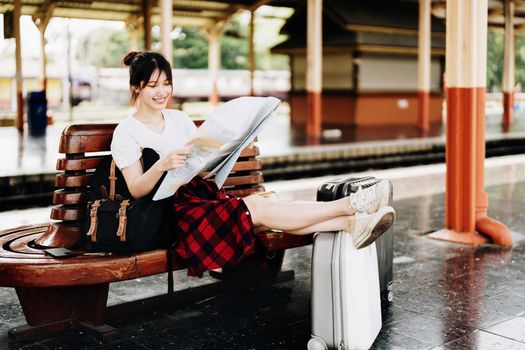 summer, relax, vacation, travel, portrait of a cute Asian girl looking at a map to plan a trip while waiting at the train station