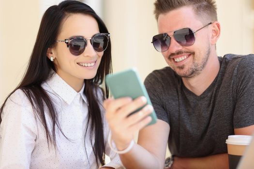 Portrait of couple watch memorable pictures on smartphone, go through pics from holiday. Man and woman smile, warm memories. Happiness, memory concept