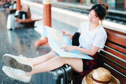 summer, relax, vacation, travel, portrait of a cute Asian girl looking at a map to plan a trip while waiting at the train station