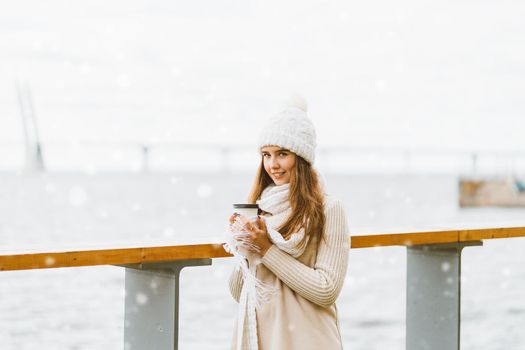Beautiful young girl drinking coffee, tea from plastic mug. Winter, Christmas eve, new year's eve. Woman with long hair is going on a vacation trip, Scandinavian style