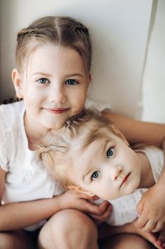 Close up of two cute little children getting fun and playing together. Adorable small girls hugging each other and looking at camera. Happy funny kids with braids spending free time and smiling.