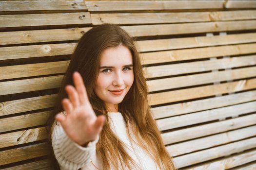 Beautiful young woman with long hair stretches her hand forward to the camera, Caucasian woman sitting on a wooden bench and pulling her arms, empty space for text