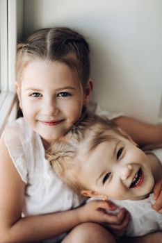 Close up of two cute little children getting fun and playing together. Adorable small girls hugging each other and looking at camera. Happy funny kids with braids spending free time and smiling.