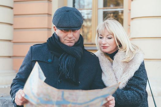 Happy blonde mature woman and handsome middle-aged brunette man travel and enjoy life. A loving couple is looking in guidebook and looking for sights, standing in a center of European city.