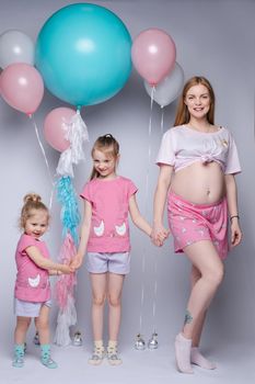 Stunning pregnant woman showing her belly. Her two daughters looking at their tummy too. They all wearing pyjamas. Studio portrait of mother and two daughters demonstrating bellies.