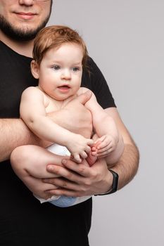 Side view of lovely father keeping little baby in hands and kissing kid on grey isolated background in studio. Happy male parent hugging and playing with child. Concept of family and love.