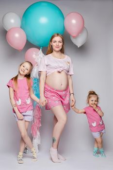 Stunning pregnant woman showing her belly. Her two daughters looking at their tummy too. They all wearing pyjamas. Studio portrait of mother and two daughters demonstrating bellies.