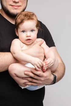 Side view of lovely father keeping little baby in hands and kissing kid on grey isolated background in studio. Happy male parent hugging and playing with child. Concept of family and love.