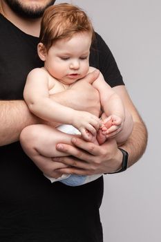 Side view of lovely father keeping little baby in hands and kissing kid on grey isolated background in studio. Happy male parent hugging and playing with child. Concept of family and love.