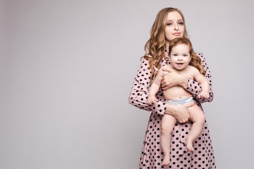 Studio portrait of gorgeous young caucasian mother holding her baby son in diaper in her arms and looking at camera. Motherhood concept. Isolate on plain background with blank space for text.