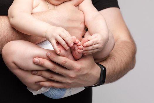 Side view of lovely father keeping little baby in hands and kissing kid on grey isolated background in studio. Happy male parent hugging and playing with child. Concept of family and love.