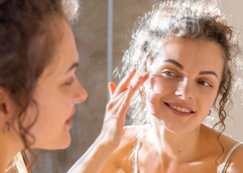 woman looking mirror applying face cream