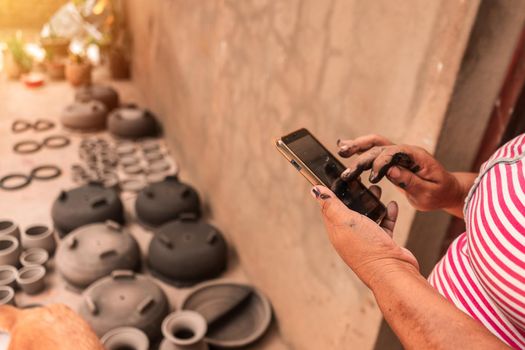 Artisan checking her cell phone to make online sales while her clay pots dry in the sun at a workshop in La Paz Centro, Nicaragua. Concept of travel, culture and economy in poor countries of America.
