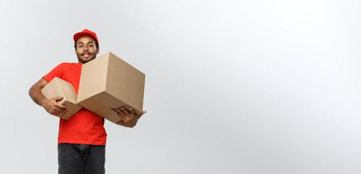 Delivery Concept - Portrait of Happy African American delivery man in red cloth holding a box package. Isolated on Grey studio Background. Copy Space