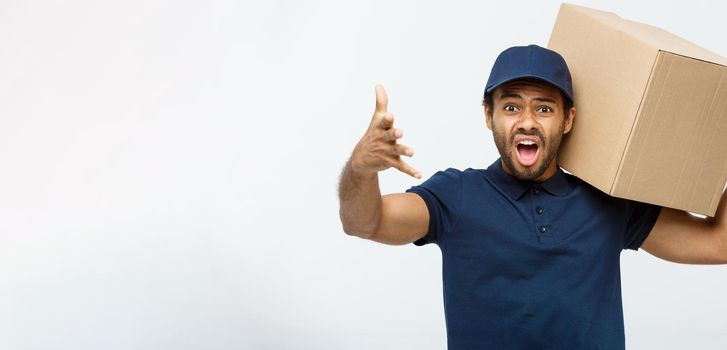 Delivery Concept - Portrait of Serious African American delivery man showing silly aggressive expression with holding a box package. Isolated on Grey studio Background. Copy Space