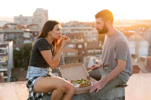 side view couple eating pizza outdoors