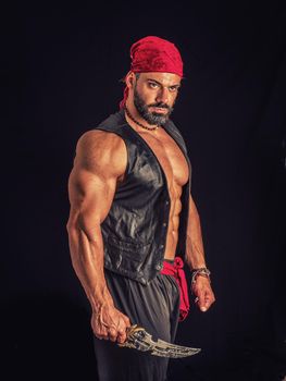 Muscular male pirate in studio shot, wearing bandana and open leather vest on naked muscle torso