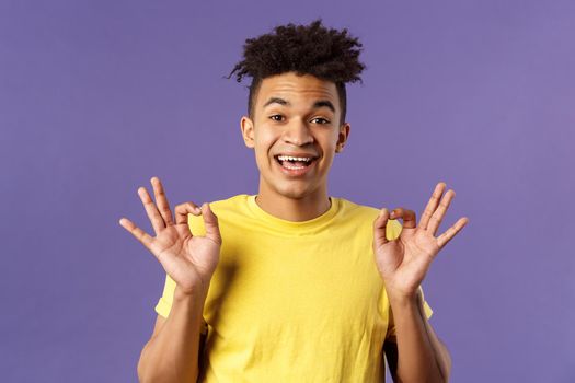 Close-up portrait of upbeat, relaxed young hipster guy with dreads assuring all good, everything be okay, show OK gesture and smiling, no problem guarantee best quality, purple background.