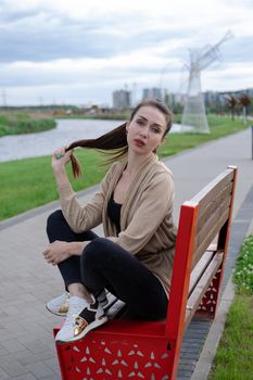 portrait of brunette woman with ponyrail sitting on a bench in park. nature lovers, attractive girl