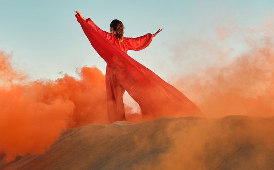 Woman in red dress dancing in the desert at blue sky