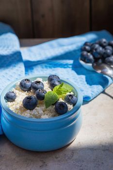 Morning fresh breakfast made from natural products from cottage cheese and blueberries. Nutritious cottage cheese and berries contain healthy vitamins. Blue background.